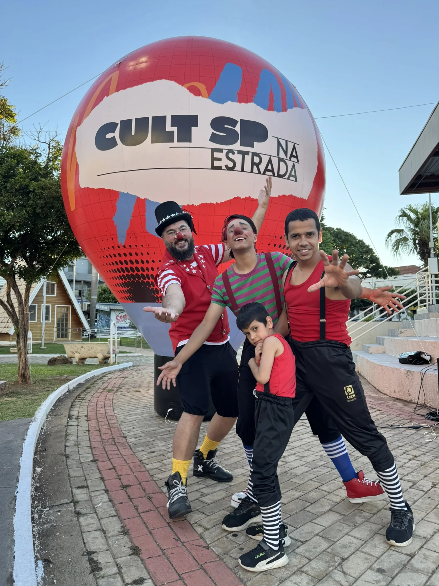 Três pessoas vestidas de palhaço na frente de um balão escrito Cult SP na estrada